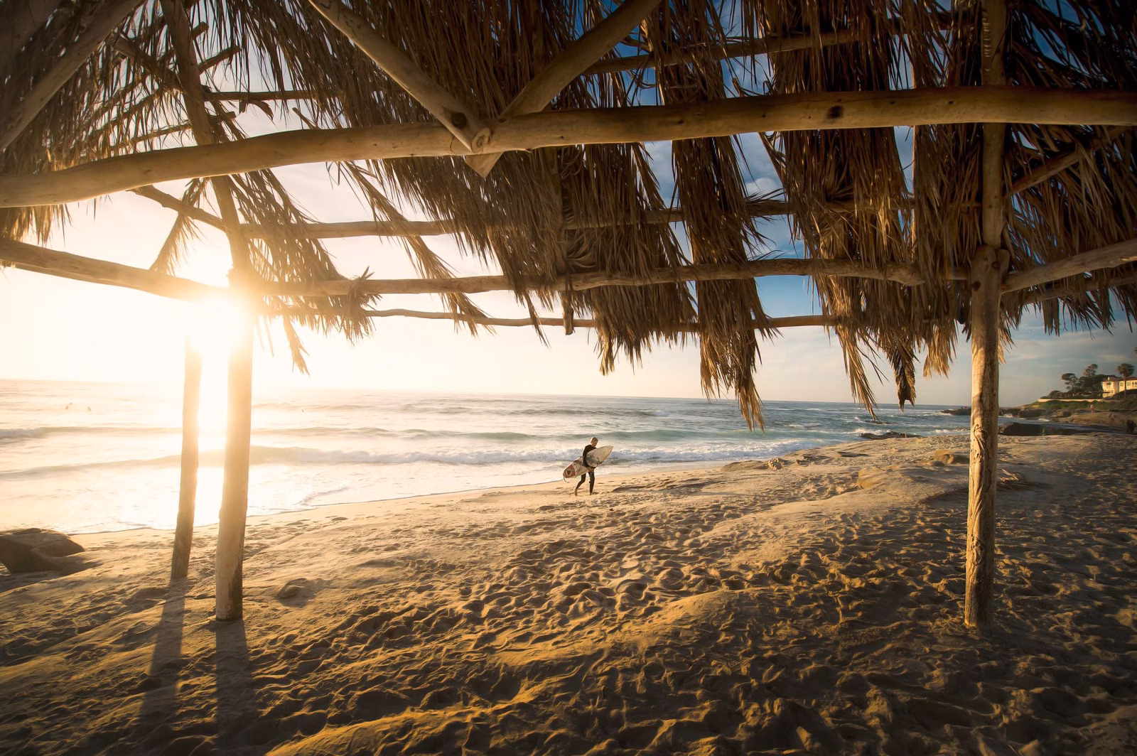 Late-afternoon sun on a sandy Southern California beach with a surfer walking to the water
