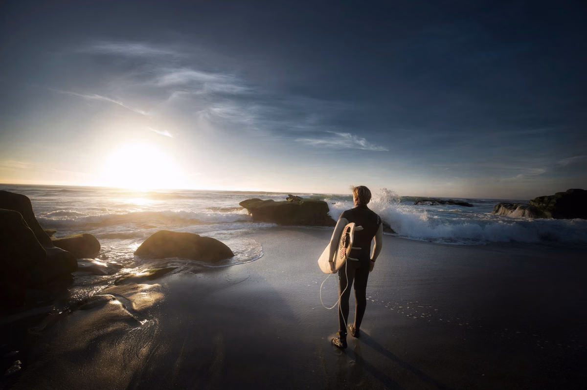 A surfer with a board watching the waves at sunrise on a Southern California beach